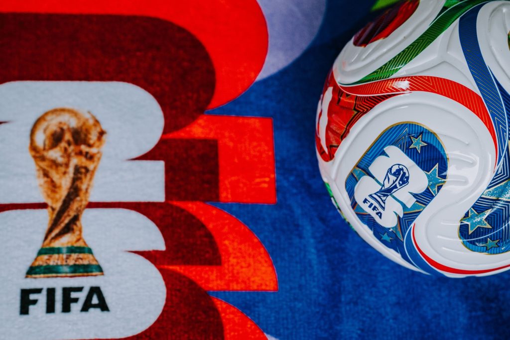FIFA themed background showing the Adidas Trionda ball and World Cup 2026 branding for the USA, Mexico, and Canada.