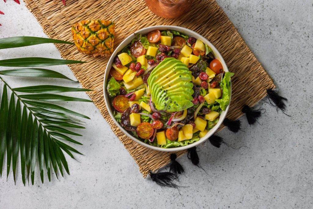 Fresh and vibrant tropical fruit salad featuring sliced avocado, mango chunks, pineapple, cherry tomatoes, and cranberries, creating a healthy and delicious meal.