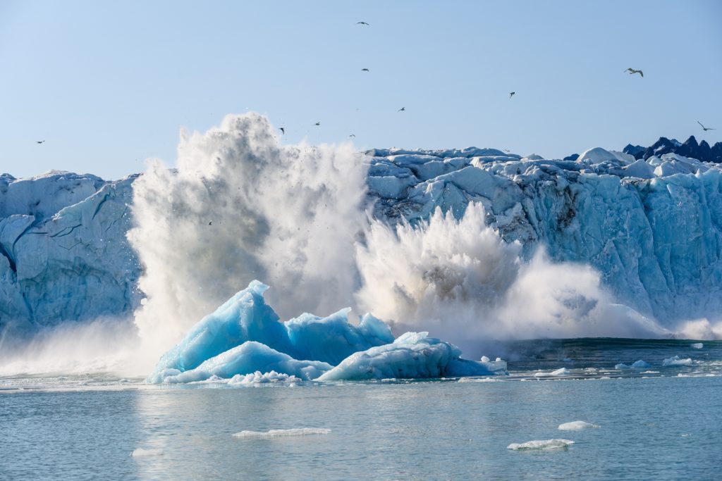 Dramatic ice calving from the Monacobreen Glacier in Liefde Fjord, small tidal wave and icebergs floating in the arctic ocean around Svalbard, signs of climate change and global warming.